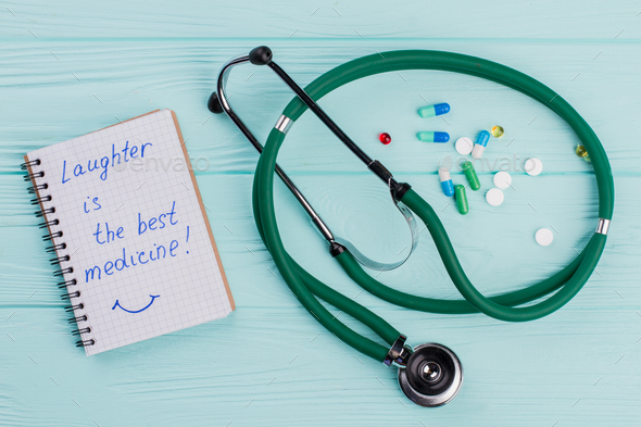 Notepad with medical stethoscope and near drug pills lying on blue background.