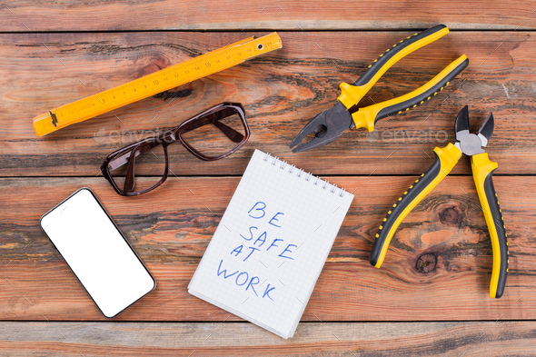 Set of carpenter working tools, smartphone, glasses on wooden textured desk.