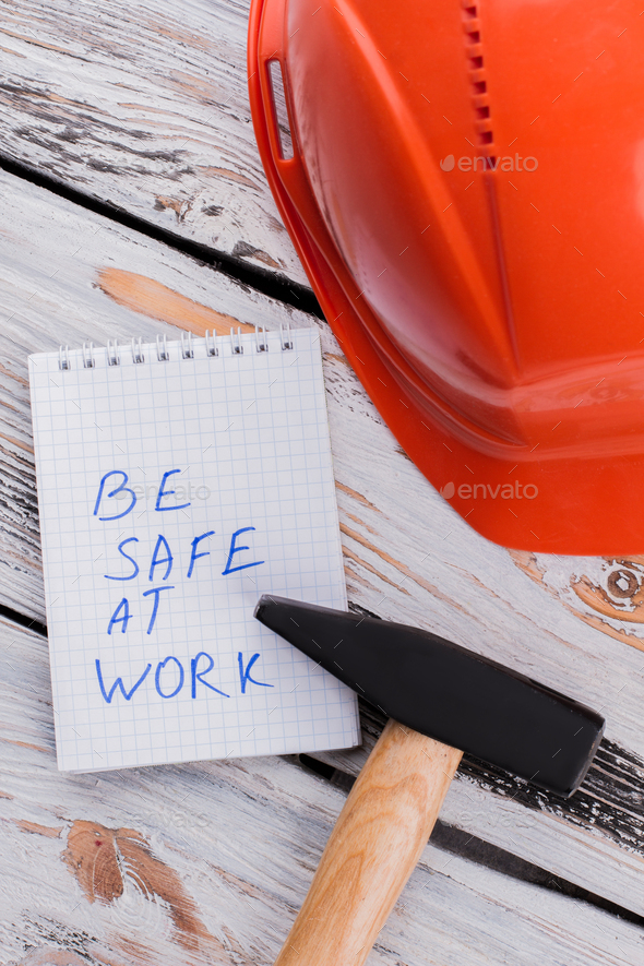 Be safe at work note with hammer and helmet on wood.