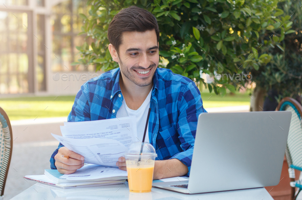 Casual European man smiling and looking happy when reading papers in cafe