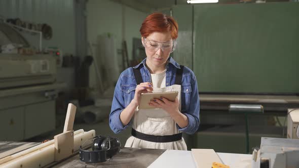 Cheerful Caucasian Female Carpenter with Red Hair Using Digital Table at Work