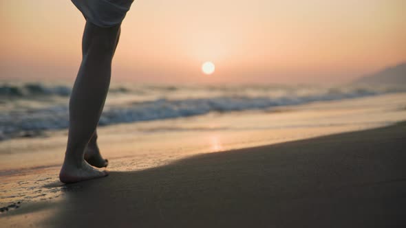 Young traveler woman with bare feet walking on the beach at sunset alt