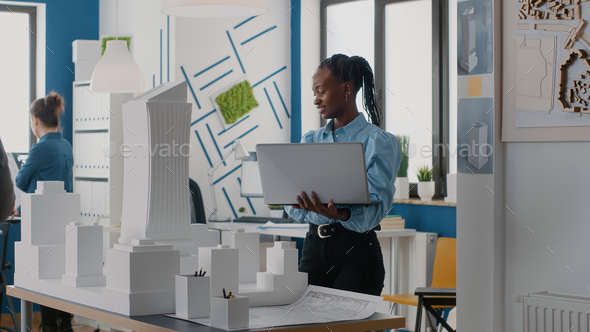 Woman architect holding laptop to analyze building model in architectural office