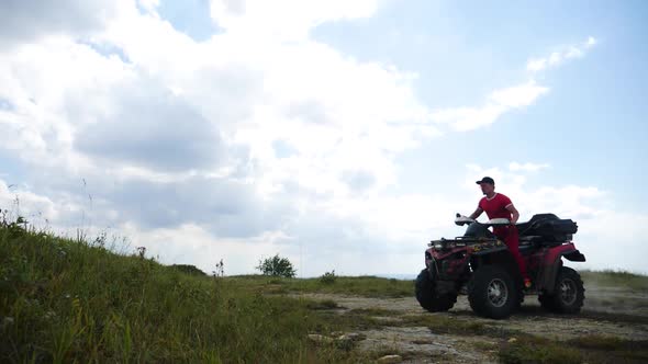 Man in a Black Cap and Red T-shirt on a Colored ATV Rides alt