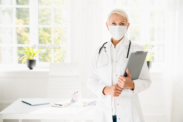 Doctor nurse in white coat face mask against coronavirus Covid 19 holding clipboard at hospital