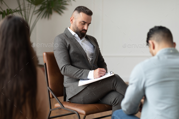 Couple sitting at therapy session with therapist, man taking notes