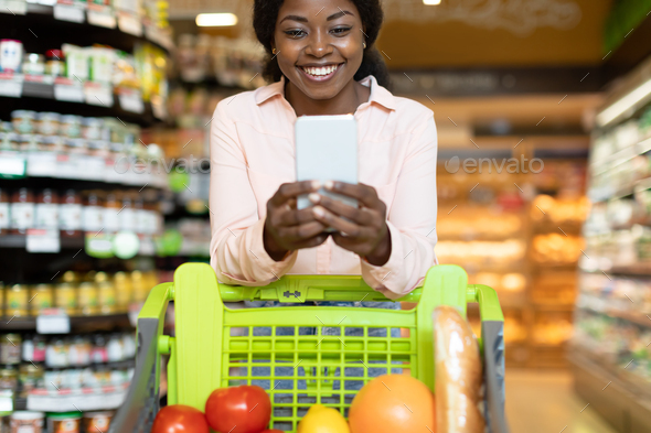 Happy Black Lady Using Phone During Grocery Shopping In Supermarket