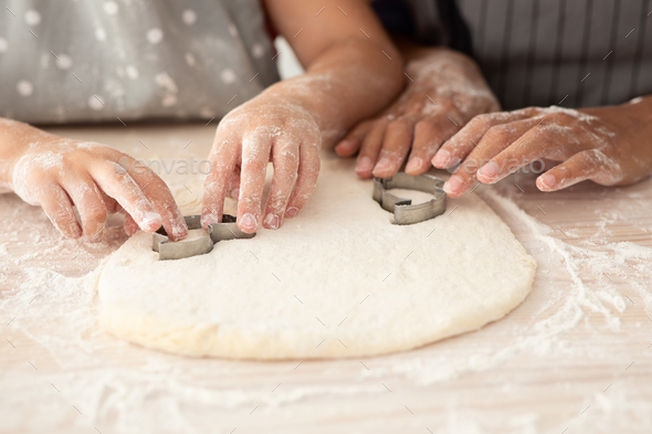 Mother And Daughter Hands Cutting Out Different Cookie Shapes Of Dough, Closeup