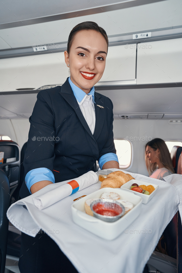 Joyful stewardess rolling airline meal trolley through aisle