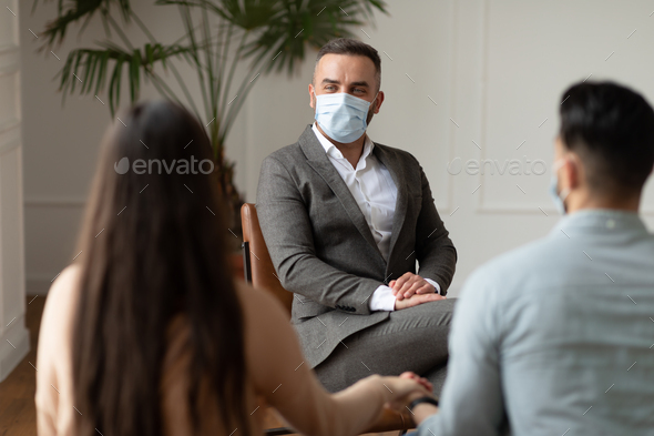 Young couple sitting at therapy session with therapist in facemask