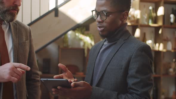 Multiethnic Male Colleagues Using Tablet and Talking in Restaurant alt