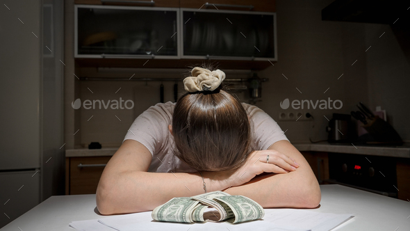 Stressed woman having to pay rent and bank loan lying on kitchen next to few money banknotes