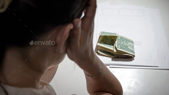 Stressed woman sitting behind desk and looking on few money banknotes to pay rent loan