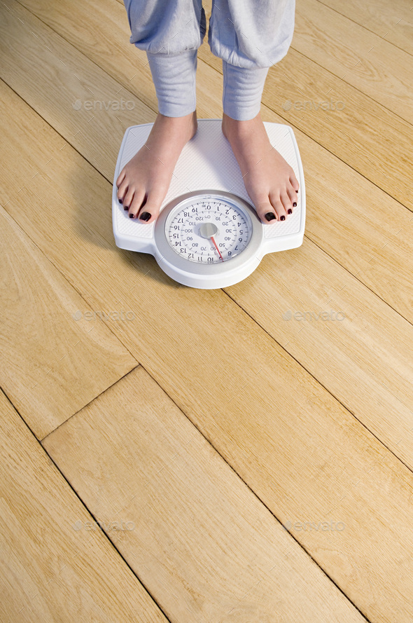 Woman standing on weighing scale, feet and lower legs. Stock Photo by