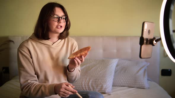 Girl food blogger spreads jam on a croissant and recording vlog on a smartphone alt