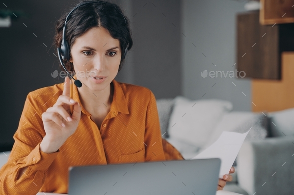 Young Spanish woman tutor wearing headset looking at laptop screen during online class