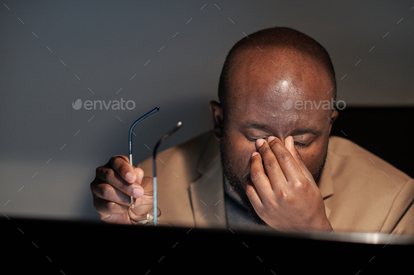 Tired African businessman rubbing his eyes during night work