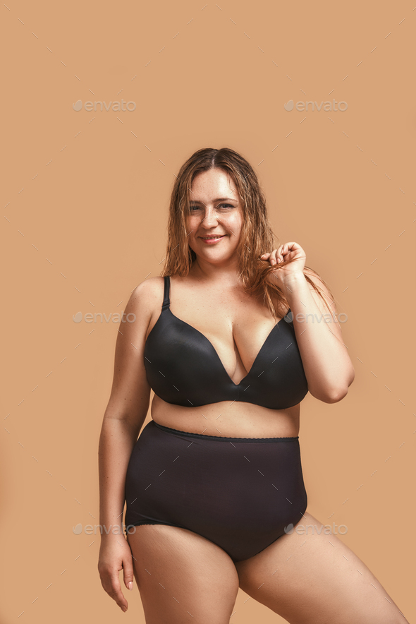 Vertical photo of plus size young woman in sexy black lingerie laughing and  posing in studio on Stock Photo by friends_stock