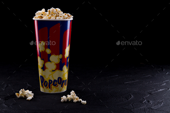Full popcorn in classic popcorn box on very dark background.