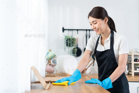 Pure clean. Young positive afro american house maid in apron cleaning table  in the modern kitchen. Professional female cleaner at work Stock Photo