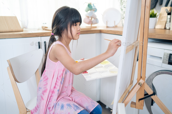 Asian young happy kid girl coloring on painting board in living room on holiday at home.
