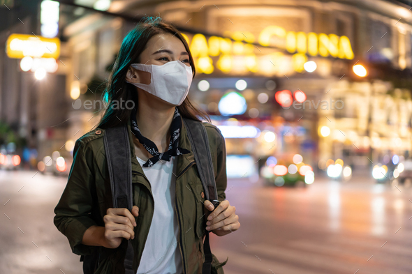 Asian attractive woman backpacker wear mask, walking in city at night enjoy spend time on holiday