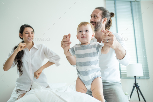 Caucasian young couple dad and mom dance with cute baby toddler enjoy morning activity after wake up