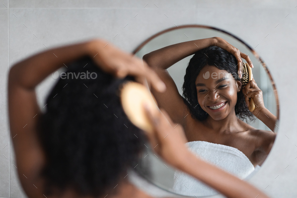 Black lady brushing hair, standing in front of mirror