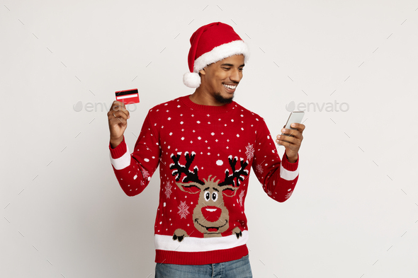 Black guy in Santa hat using smartphone, holding credit card