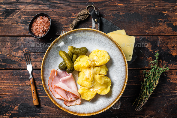 Melted Raclette Swiss cheese with boiled potato and ham. Wooden background. Top view