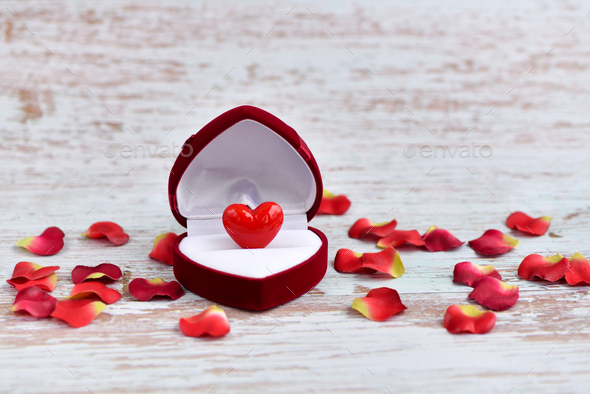 Open heart-shaped gift box with glass heart with petals on a light wooden background - Stock Photo - Images