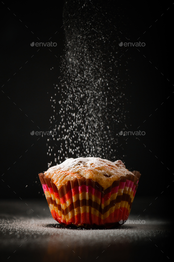 The cook sprinkles muffin with powdered sugar on a black background. The process of making cake