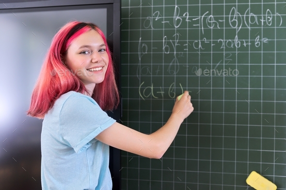 Female student teenager at a math lesson writing in chalk on a blackboard