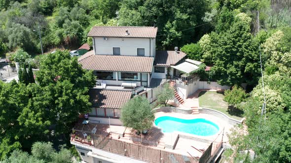 Slow aerial dolly of small Mediterranean villa with pool surrounded by trees alt