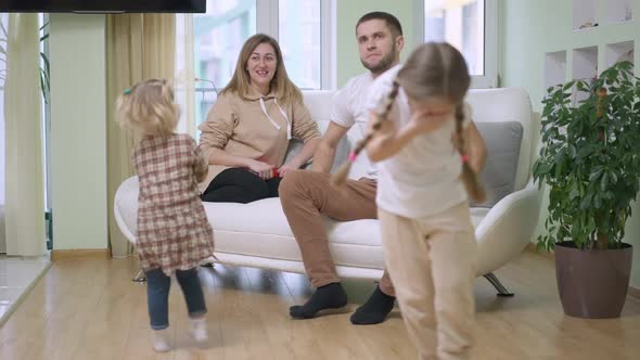 Happy Caucasian Woman Sitting on Couch Looking at Children Spinning in Slow Motion As Man Scolding alt