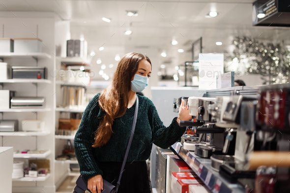 Cheerful lady in face mask chooses coffee machine in shopping mall during covid19 pandemic