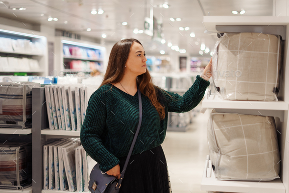Young focused woman doing shopping in store mall in bedding department
