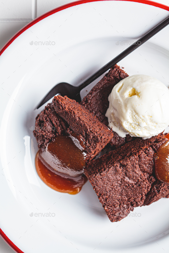 Vegan brownie squares with a scoop of dairy-free ice cream and apple caramel in white plate.