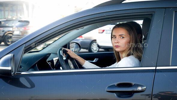 Portrait of young female driver looking out the open window while driving a car - Stock Photo - Images