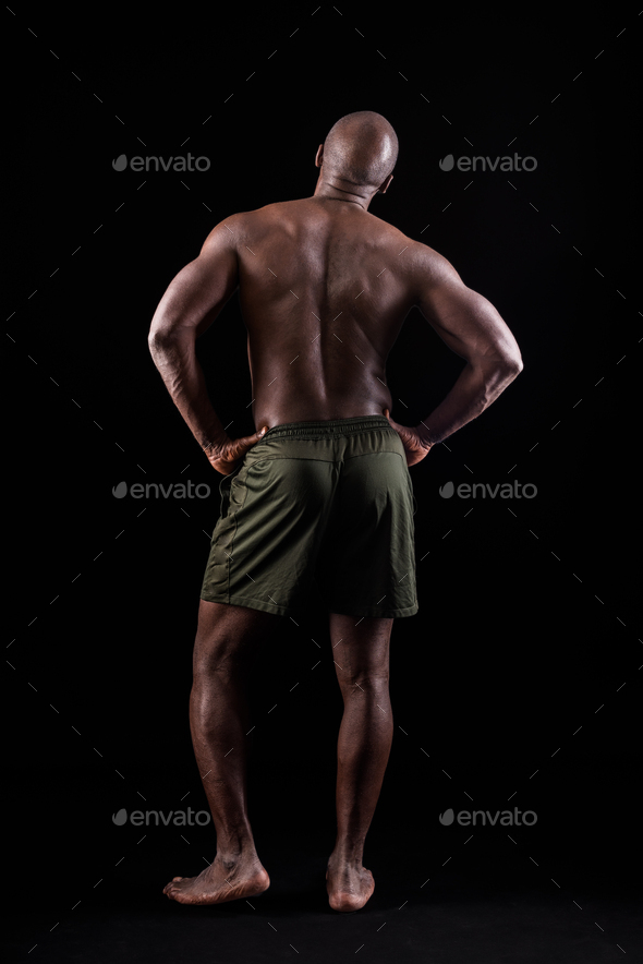 Back view of a muscular man standing with his hands on his waist