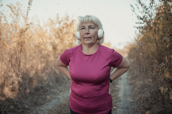 Elderly runner woman working with headphones and smart watch