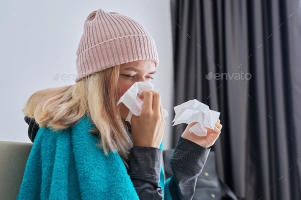 Teenager girl sneezing in handkerchief, female with symptoms of illness sitting at home