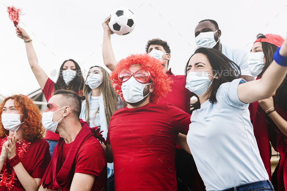 Friends wearing protective face mask screaming and watching soccer match at stadium