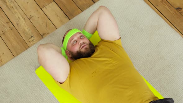 Fat Man in Yellow Sportswear Doing Abs Exercise Crunches at Home Lying on Mat