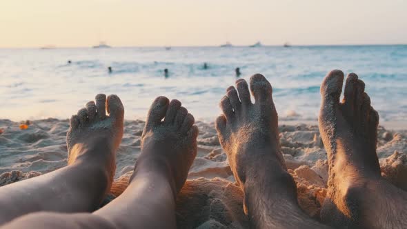 POV Feet of a Couple of Men and Women Lying on a Sandy Beach at Sunset By Ocean alt