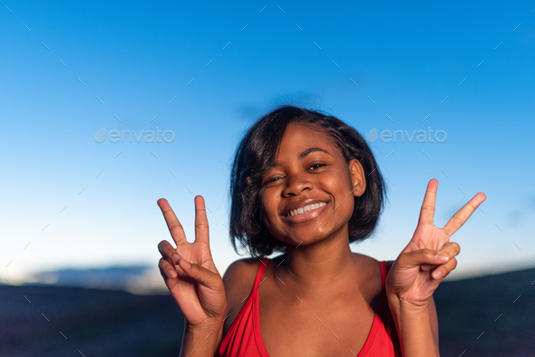 Smiling black woman gesturing victory with the hands during sunset