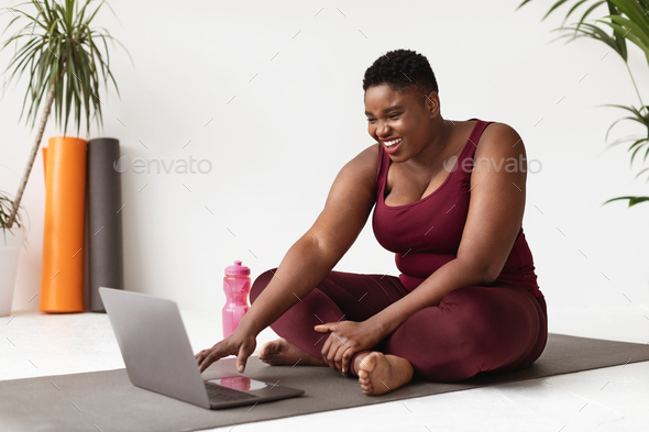 Positive overweight african american woman enjoying remote workout Stock  Photo by Prostock-studio
