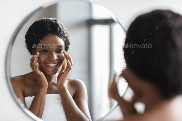 Mirror reflection of happy black lady applying eye care product
