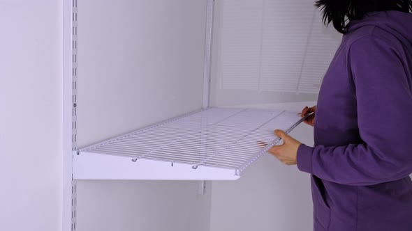 Installation of a metal mesh shelf in the dressing room system on a bracket. A woman in a purple hoo alt