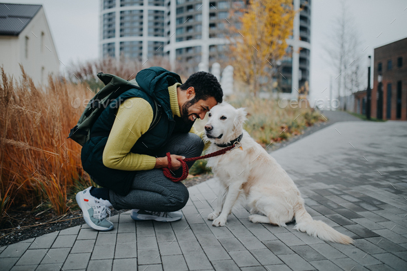 Happy young man squatting and embracing his dog during walk outdoors in city - Stock Photo - Images